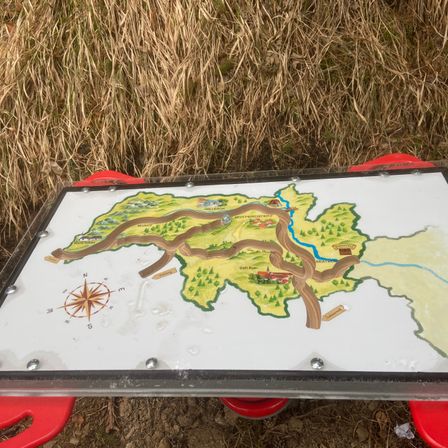 Eine Outdoor-Kartenanzeige, auf einem roten Ständer platziert, zeigt den Weg eines Flusses durch eine ländliche Landschaft.