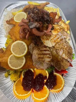 Eine große Platte mit verschiedenen Fleischsorten, einschließlich Würsten, Hähnchen und Schweinekoteletts, garniert mit Zitronenscheiben und Orangenscheiben mit Marmelade.