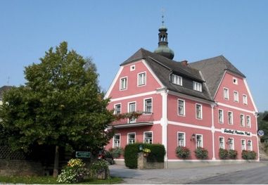 Ein rotes Gebäude mit grauem Dach und mehreren Fenstern, umgeben von Grün und Blumen. Das Schild heißt 'Gasterl Pension'.
