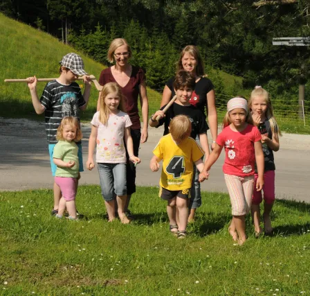 Eine Familie von acht Personen, zwei Erwachsene und sechs Kinder, geht barfuß auf Gras, mit zwei Erwachsenen in der Mitte und Kindern um sie herum.
