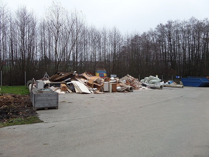 Ein leerstehendes Grundstück mit einem Haufen Schutt, darunter Holz, Plastik und Metall. Ein blauer Container steht rechts.