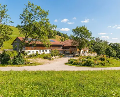 Ein großes Haus mit Solarpanelen auf dem Dach ist von einem üppigen grünen Feld und Bäumen umgeben.