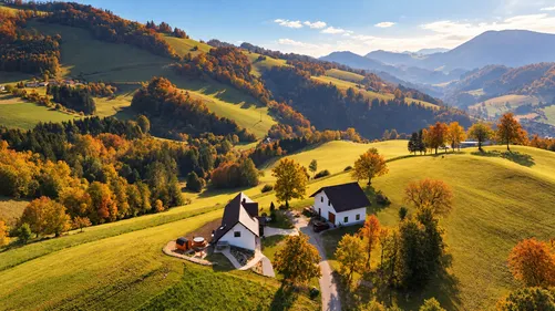 Ein Luftbild einer friedlichen Landschaft mit einem Haus, umgeben von üppigen grünen Feldern, Bäumen und Bergen.