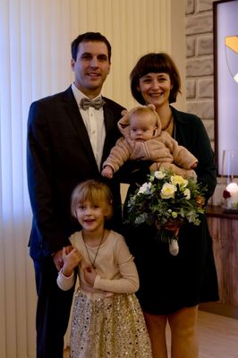 Eine vierköpfige Familie, bestehend aus einem Mann, einer Frau, einem Baby und einem jungen Mädchen, lächelt und posiert für ein Foto. Die Frau hält einen Blumenstrauß und das Baby trägt einen Bärenkostüm.