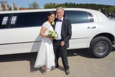 Ein frisch verheiratetes Paar steht vor einer weißen Limousine, der Bräutigam trägt eine Fliege und die Braut hält einen Blumenstrauß.