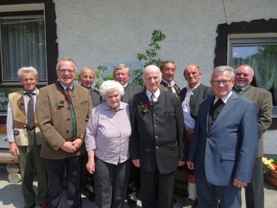 Eine Gruppe älterer Personen in traditioneller Kleidung, die vor einem Gebäude mit einer Pflanze in der Mitte stehen.