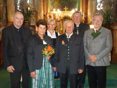 Eine Gruppe von Menschen in traditioneller Kleidung posiert für ein Foto vor einem Kirchenaltar mit Kerzen und einem Kreuz.