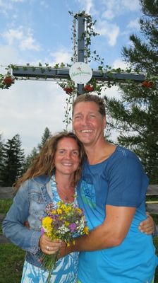 Ein Mann und eine Frau lächeln und posieren für ein Foto mit einem Blumenstrauß vor einem Holzzaun und einem Schild mit der Aufschrift Naturfreunde.