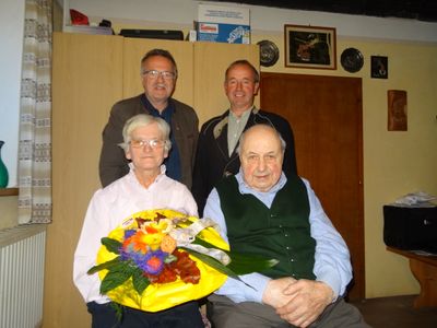 Vier Männer in einem Raum mit einer Frau, die einen Blumenstrauß hält. Zwei Männer stehen hinter ihnen.