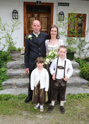Eine Familie von vier Personen, gekleidet in traditioneller Kleidung, steht auf einer Steintreppe vor einem Haus und lächelt für ein Foto.