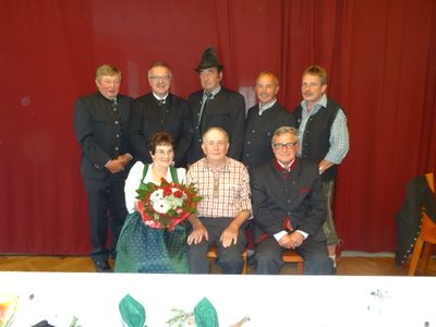 Eine Gruppe von Erwachsenen, sowohl Männer als auch Frauen, gekleidet in traditioneller Kleidung, posiert für ein Foto vor einem roten Vorhang.