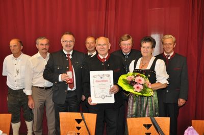 Eine Gruppe von Menschen in formeller Kleidung, die vor einem roten Vorhang stehen und ein Zertifikat und Blumen halten.