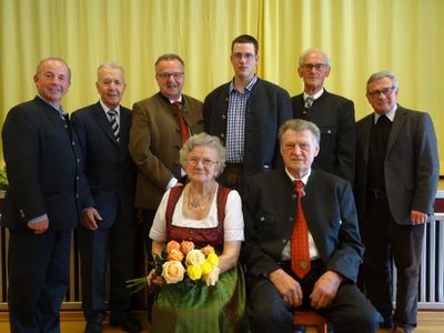 Eine Gruppe von Menschen, darunter Männer und Frauen, steht und sitzt vor einem gelben Vorhang und lächelt für ein Foto.