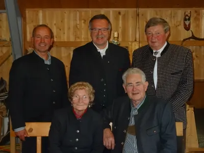 Fünf Personen, darunter drei Männer und zwei Frauen, stehen zusammen vor einer Holzwand. Sie alle scheinen für die Kamera zu lächeln.