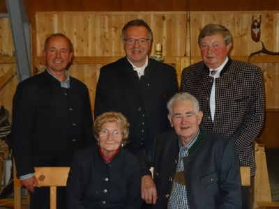 Fünf Personen, darunter drei Männer und zwei Frauen, stehen zusammen vor einer Holzwand. Sie alle scheinen für die Kamera zu lächeln.