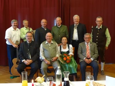 Eine Gruppe älterer Männer und Frauen in traditioneller Kleidung posiert für ein Foto mit Musikinstrumenten im Hintergrund.