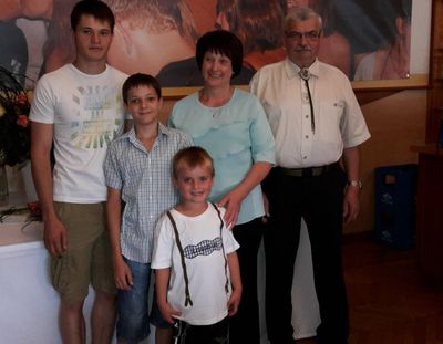 Eine Familie mit fünf Personen, darunter zwei Jungen, eine Frau und zwei Männer, posiert für ein Foto vor einem großen Gemälde.