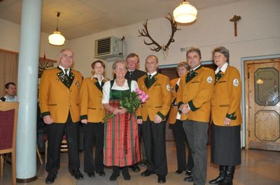 Eine Gruppe von Menschen in traditionellen gelben und grünen Uniformen steht in einem Raum mit einer Holztür und einem Kreuz an der Wand.