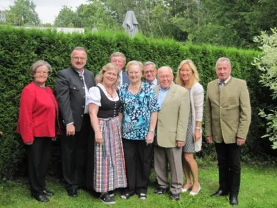 Eine Gruppe von Menschen, darunter Männer und Frauen, steht lächelnd und posiert für ein Foto vor einer Hecke.