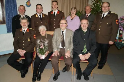 Eine Gruppe von Menschen in Uniformen und Anzügen posiert für ein Foto, wobei eine Frau einen Blumenstrauß hält.