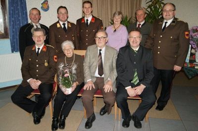 Eine Gruppe von Menschen in Uniformen und Anzügen posiert für ein Foto, wobei eine Frau einen Blumenstrauß hält.