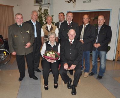 Eine Gruppe von Menschen in formeller Kleidung, darunter eine Frau mit einem Blumenstrauß, posiert für ein Foto in einem Raum.