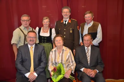 Eine Gruppe von Menschen, darunter eine Frau mit Blumen, posiert für ein Foto vor einem roten Vorhang.