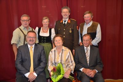 Eine Gruppe von Menschen, darunter eine Frau mit Blumen, posiert für ein Foto vor einem roten Vorhang.