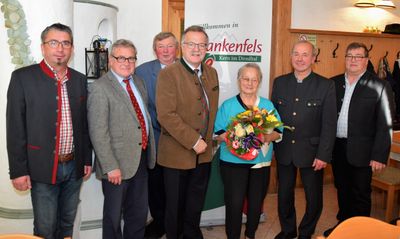 Fünf Männer und eine Frau stehen vor einem Banner mit dem Text 'Willkommen in Bankenfels'. Die Frau hält einen Blumenstrauß.