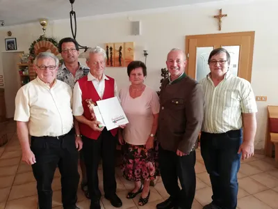 Eine Gruppe von Menschen steht in einem Raum, ein Mann hält eine Trophäe und ein Zertifikat.