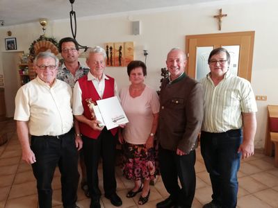 Eine Gruppe von Menschen steht in einem Raum, ein Mann hält eine Trophäe und ein Zertifikat.
