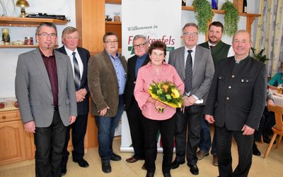 Eine Gruppe von Männern und einer Frau steht vor einem Banner, das 'Willkommen in Fürkenfels' sagt. Sie sind alle formell gekleidet und scheinen für ein Foto zu posieren.