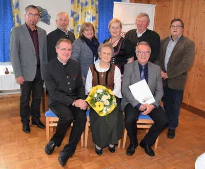 Eine Gruppe von Menschen, darunter eine Frau in traditioneller Kleidung, posiert für ein Foto in einem Raum mit Holzböden und einem Banner im Hintergrund.