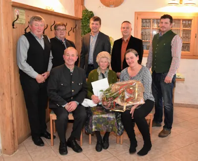 Eine Gruppe von Menschen steht und sitzt in einem Raum, eine Frau hält einen Blumenstrauß und ein Zertifikat.