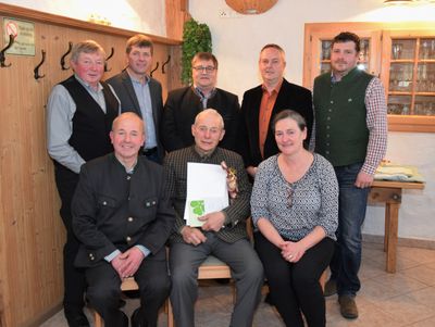 Eine Gruppe von Menschen posiert für ein Foto, wobei ein Mann in der Mitte ein Papier und ein grünes vierblättriges Kleeblatt hält.