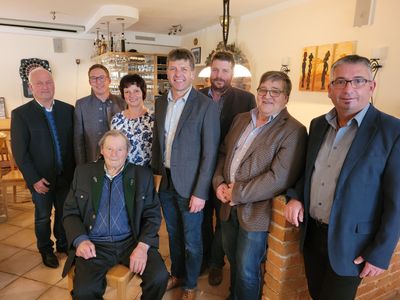 Eine Gruppe von Menschen, darunter Männer und Frauen, steht lächelnd für ein Foto in einem Raum mit einer Ziegelwand und Gemälden an der Wand.