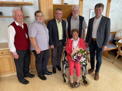 Eine Gruppe von Männern und eine ältere Frau im Rollstuhl, alle lächeln und posieren für ein Foto in einem Raum.