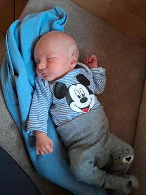 Ein Baby in einem blauen Mickey Mouse-Shirt und grauen Hosen schläft auf einer blauen Decke.