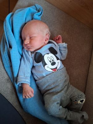 Ein Baby in einem blauen Mickey Mouse-Shirt und grauen Hosen schläft auf einer blauen Decke.