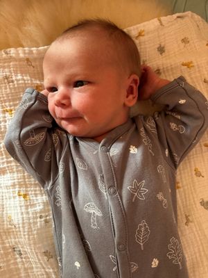 Ein Baby liegt auf einer Decke mit einem Blatt- und Pilzdruck auf seinem Pyjama und schaut mit leicht geöffnetem Mund nach oben.