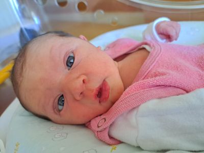Ein Baby mit blauen Augen und einer rosa Kleidung liegt auf einem weißen Tuch mit einem unscharfen Hintergrund.