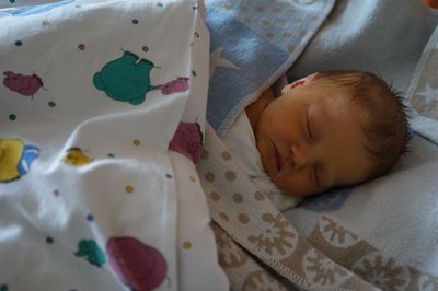 Ein Baby schläft friedlich unter einer blauen Decke mit einer weißen Decke, die bunte Cartoon-Figuren zeigt.
