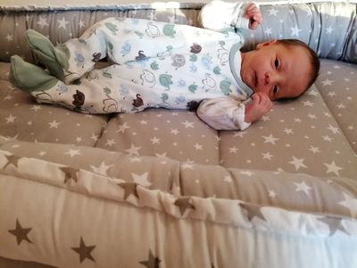 Ein Baby liegt auf einem mit Sternen bedruckten Bett, trägt Pyjamas mit Elefanten-Aufdrucken und schaut direkt in die Kamera.