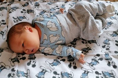 Ein Baby liegt auf einem Bett mit einer Micky-Maus-Bettdecke und trägt Pyjamas mit Elefantenmuster.