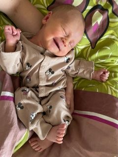 Ein Neugeborenes in Mickey-Mouse-Pyjamas schläft auf einem Bett mit einer bunten Decke.