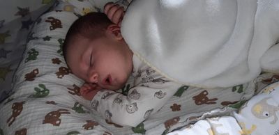 Ein Baby schläft friedlich auf einem Bett, bedeckt mit einer weißen Decke, in einem Pyjama mit Affendruck.