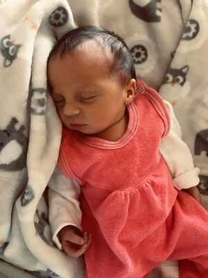 Ein Babymädchen schläft friedlich, eingewickelt in ein rosa Kleid und eine weiße Decke mit einem grau-weißen Eulenmuster.