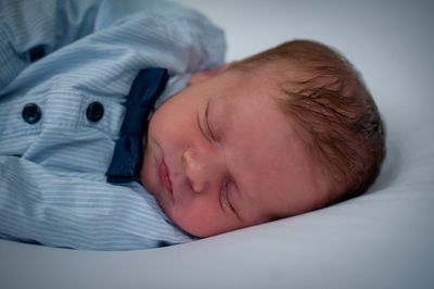 Ein Babyjunge in einem blau gestreiften Hemd mit einer marineblauen Schleife schläft friedlich auf einer weißen Oberfläche.