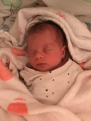 Ein Neugeborenes schläft friedlich, eingewickelt in eine weiße Decke mit Sternen. Die Augen des Babys sind geschlossen, und es sieht friedlich aus.