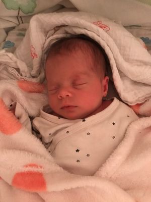 Ein Neugeborenes schläft friedlich, eingewickelt in eine weiße Decke mit Sternen. Die Augen des Babys sind geschlossen, und es sieht friedlich aus.